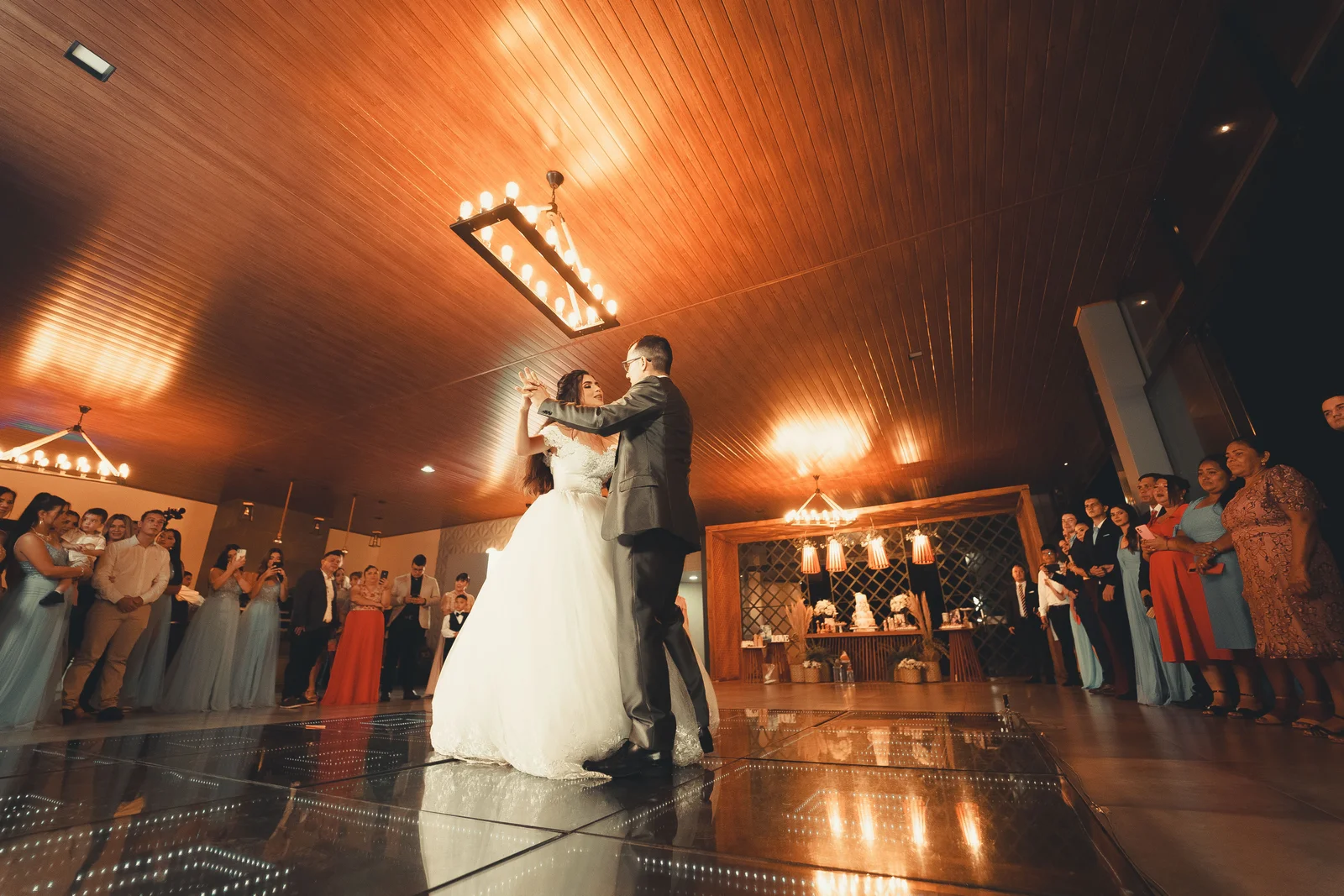 Una pareja de recién casados comparte su primer baile, rodeada de invitados.